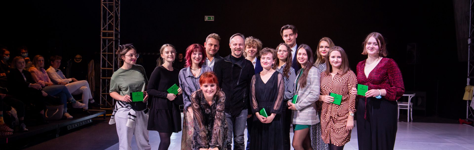 Grupowe zdjęcie studentów z wykładowcami na scenie, studenci trzymają w dłoniach zielone indeksy