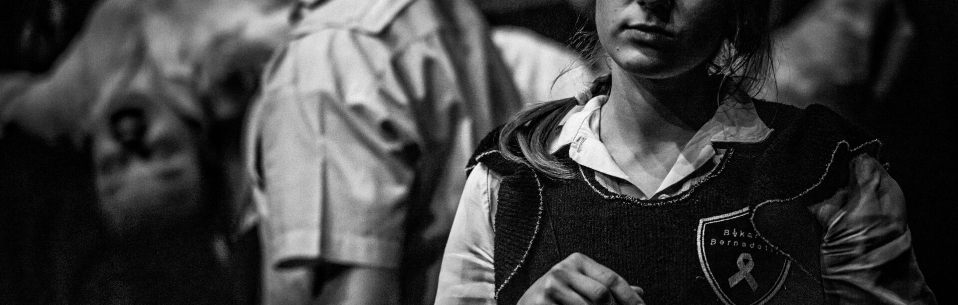 Kobieta na pierwszym planie miesza coś w metalowym kubku. Na drugim planie rozmyte ciała dzieci znęcających się nad swoją koleżanką.