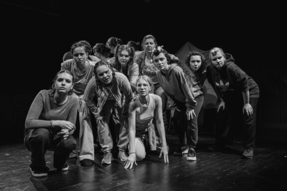 Grupa ludzi, w różnych pozycjach, patrzą w jednym kierunku.