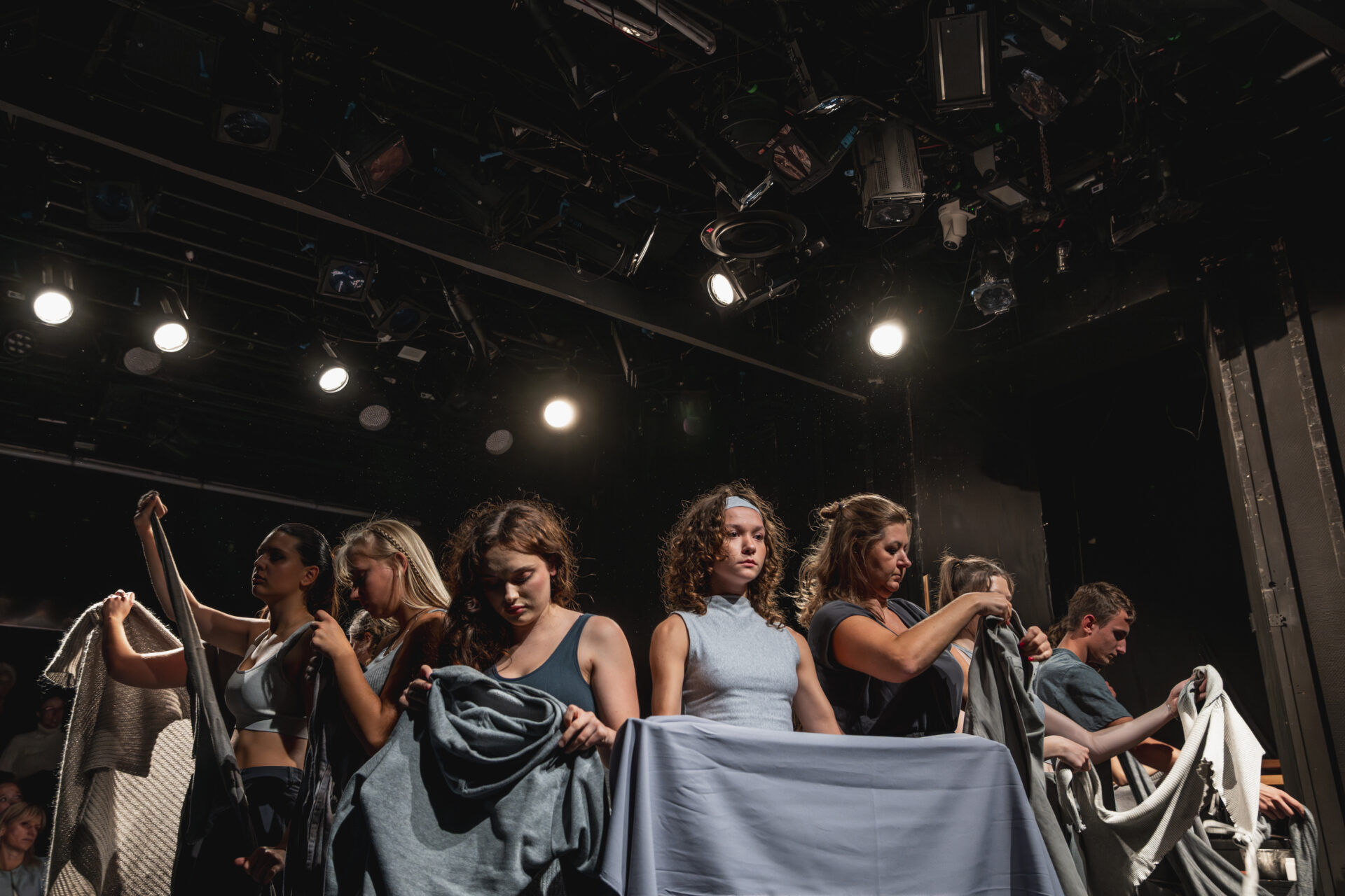 W kole, plecami do środka koła stoją różne osoby, wyglądają jakby każdy rozbierał inny element swojej garderoby.