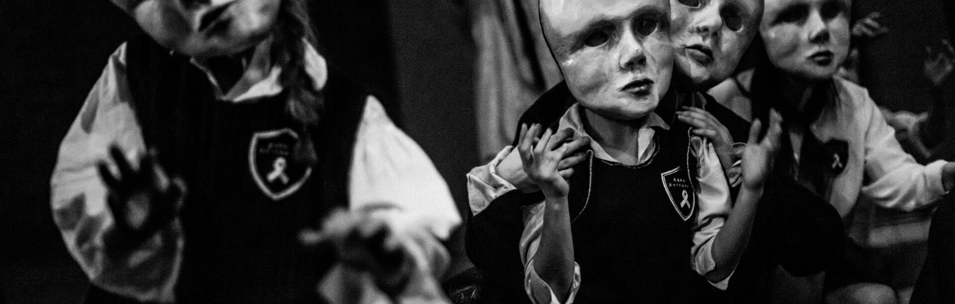 Kilka postaci w różnych pozycjach, każda ma na głowie dużą dziecięcą maskę.